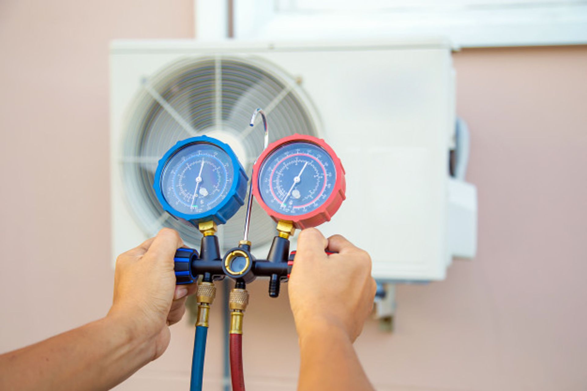 A person is holding two gauges in front of an air conditioner.