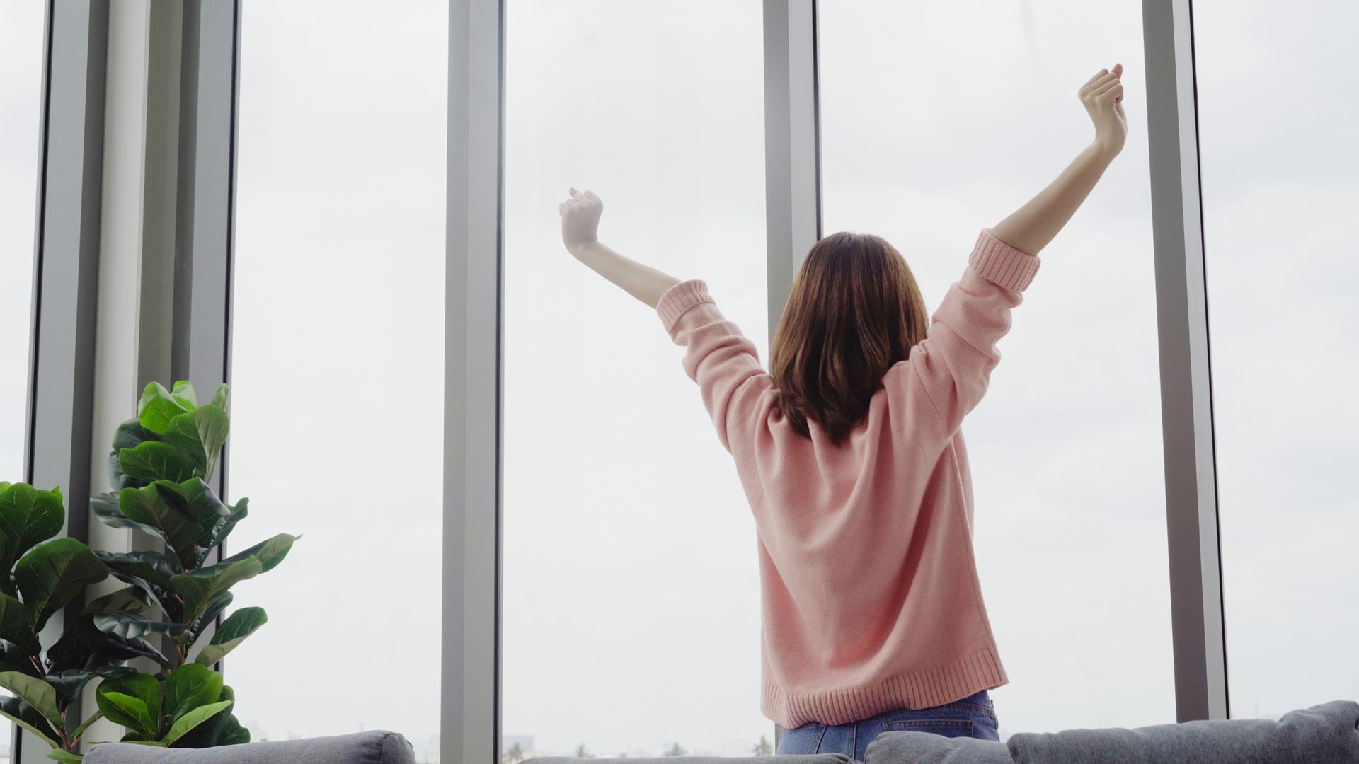 A woman is sitting on a couch with her arms outstretched in front of a window.
