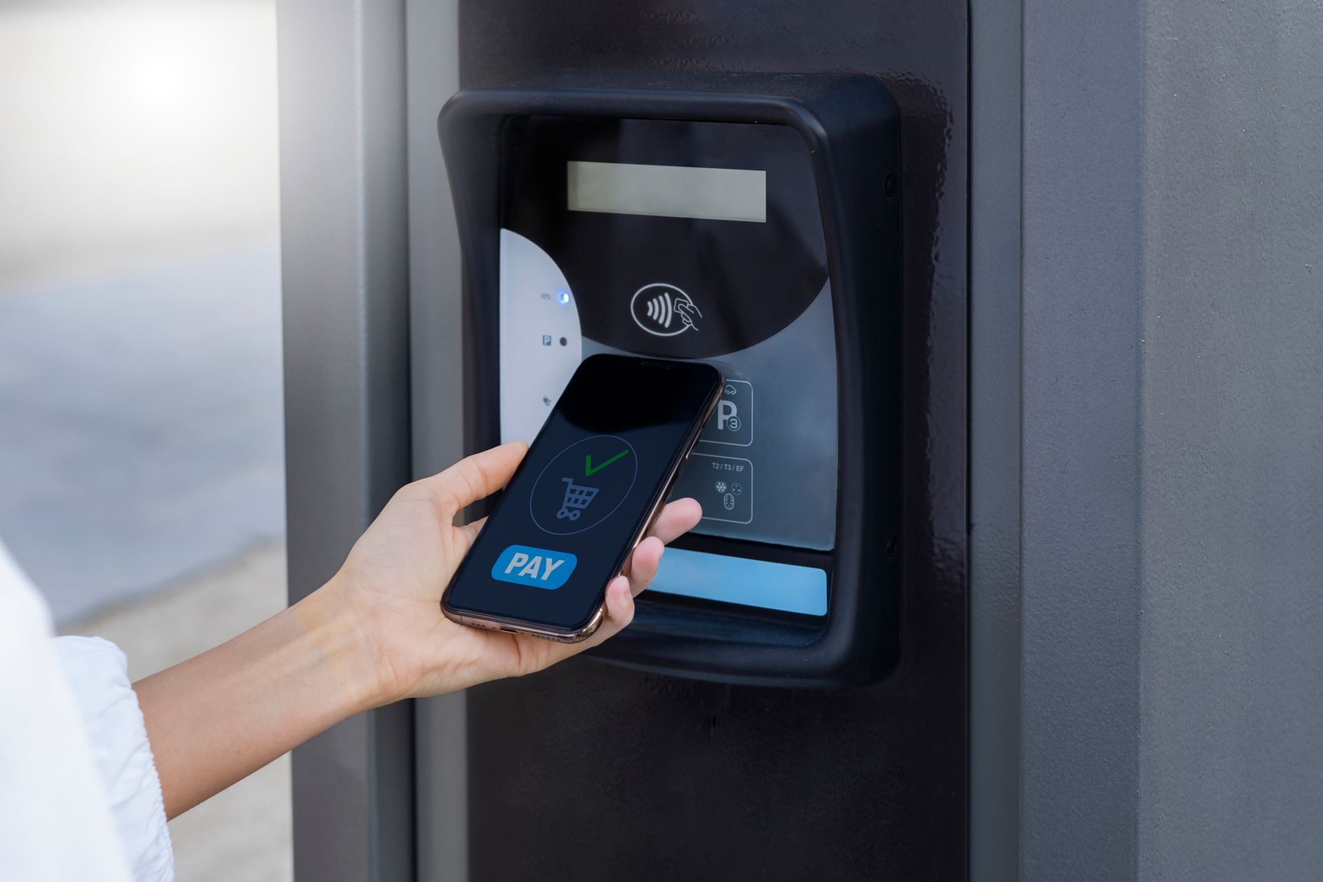 Person using a smartphone to tap a wall-mounted access reader with a blue-lit display.