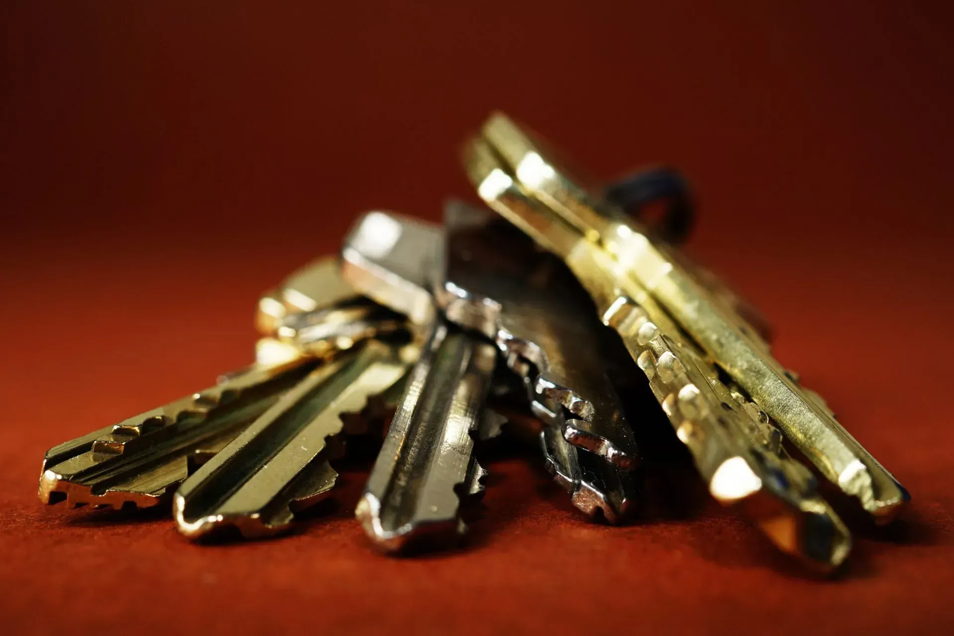 A small pile of metallic house keys on a red surface with a blurred background