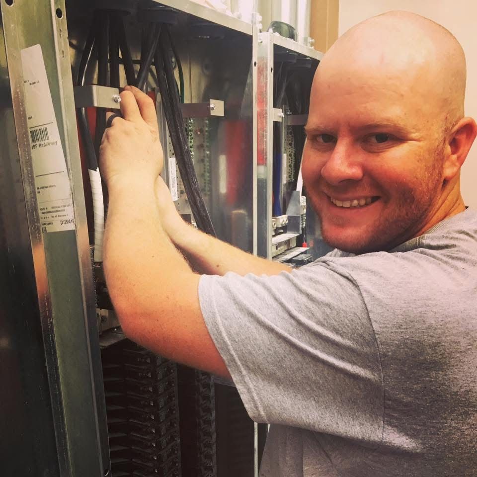 An electrician is working on an electrical panel with a multimeter.