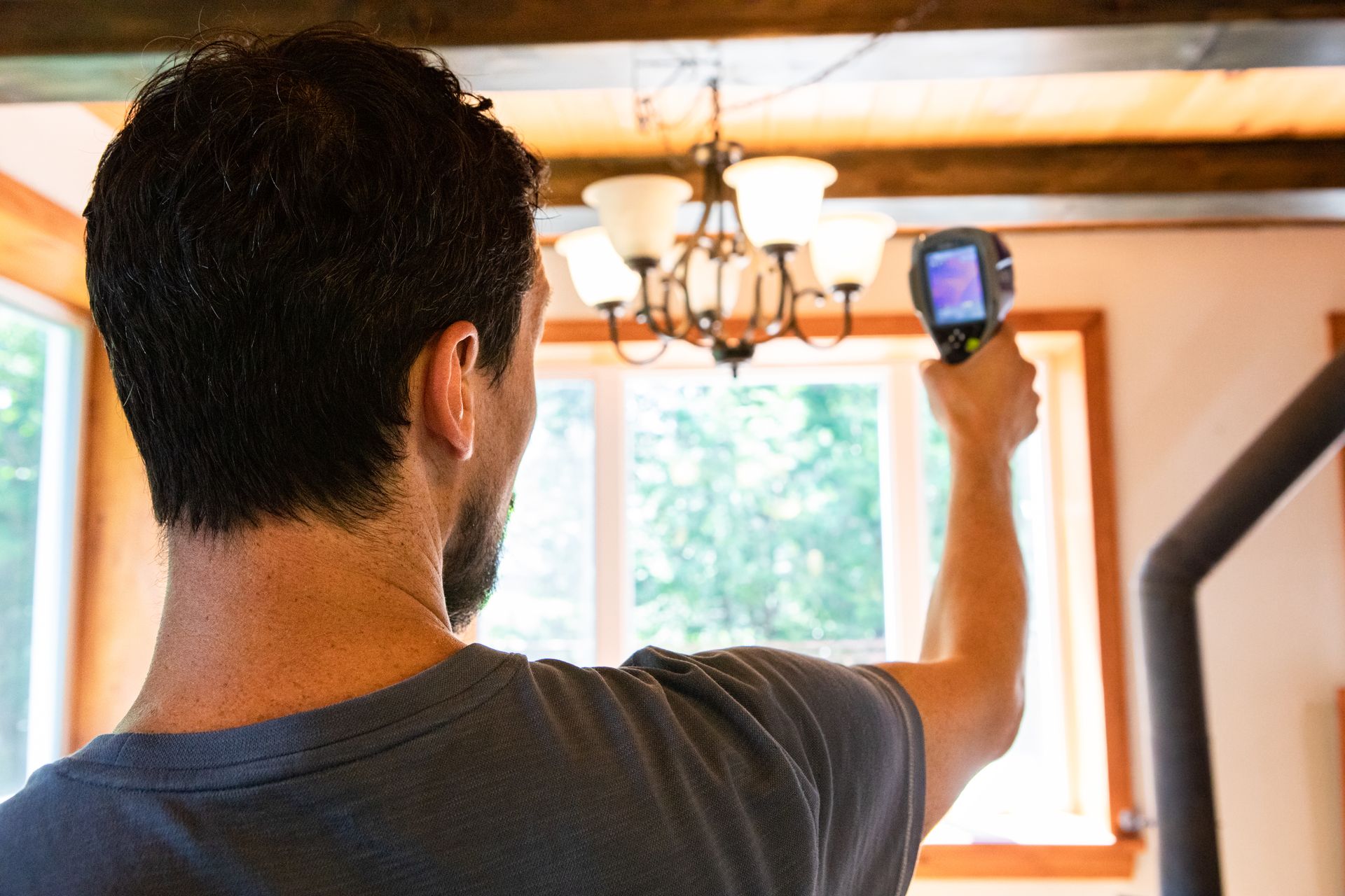 Person using a thermal imaging camera inside a home, aiming towards a window.