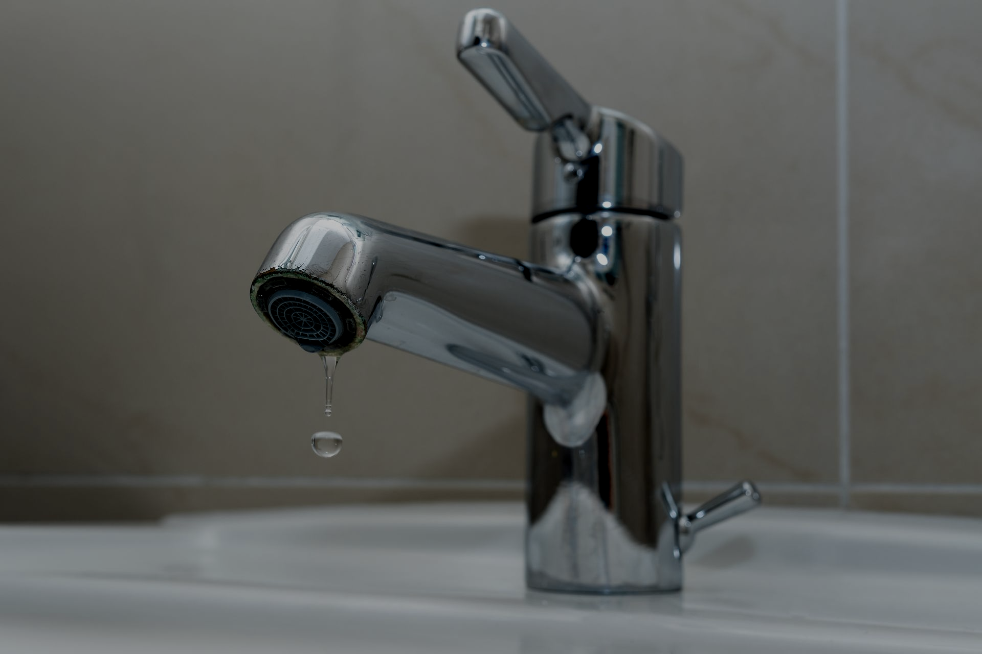 Chrome faucet dripping water into a white sink.