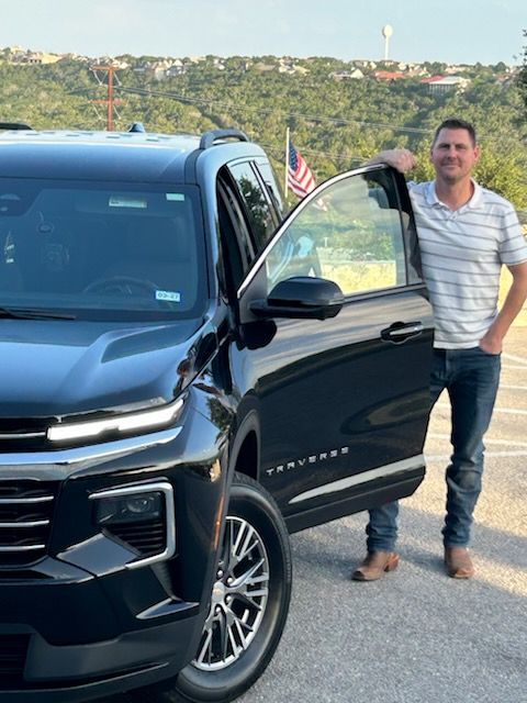 Tim is standing in front of a black Chevy Traverse with the door open.