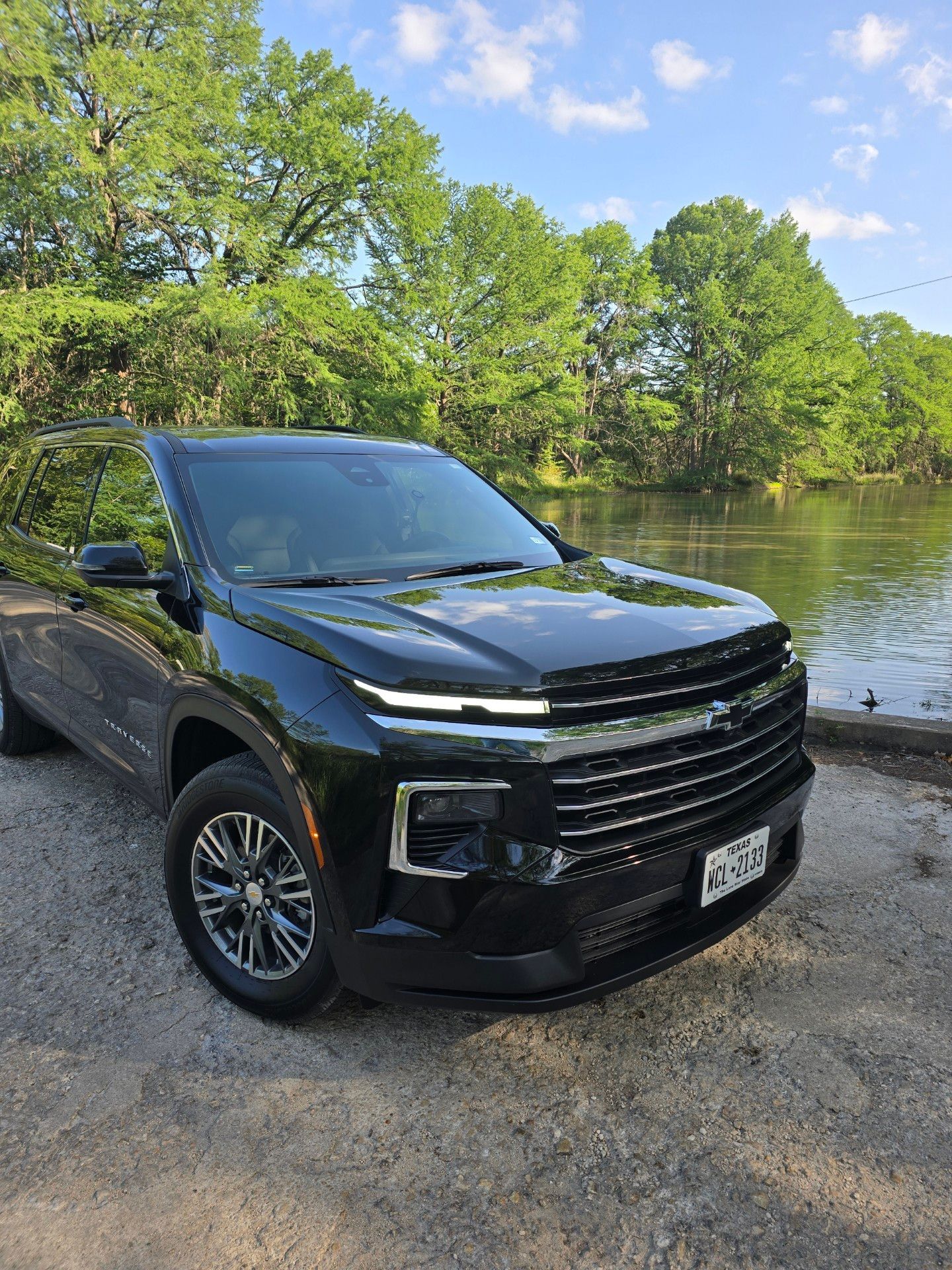 A black Chevy Traverse is parked next to a body of water.