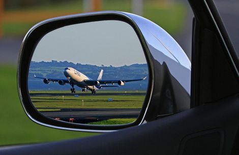 A rear view mirror shows an airplane taking off from an airport runway