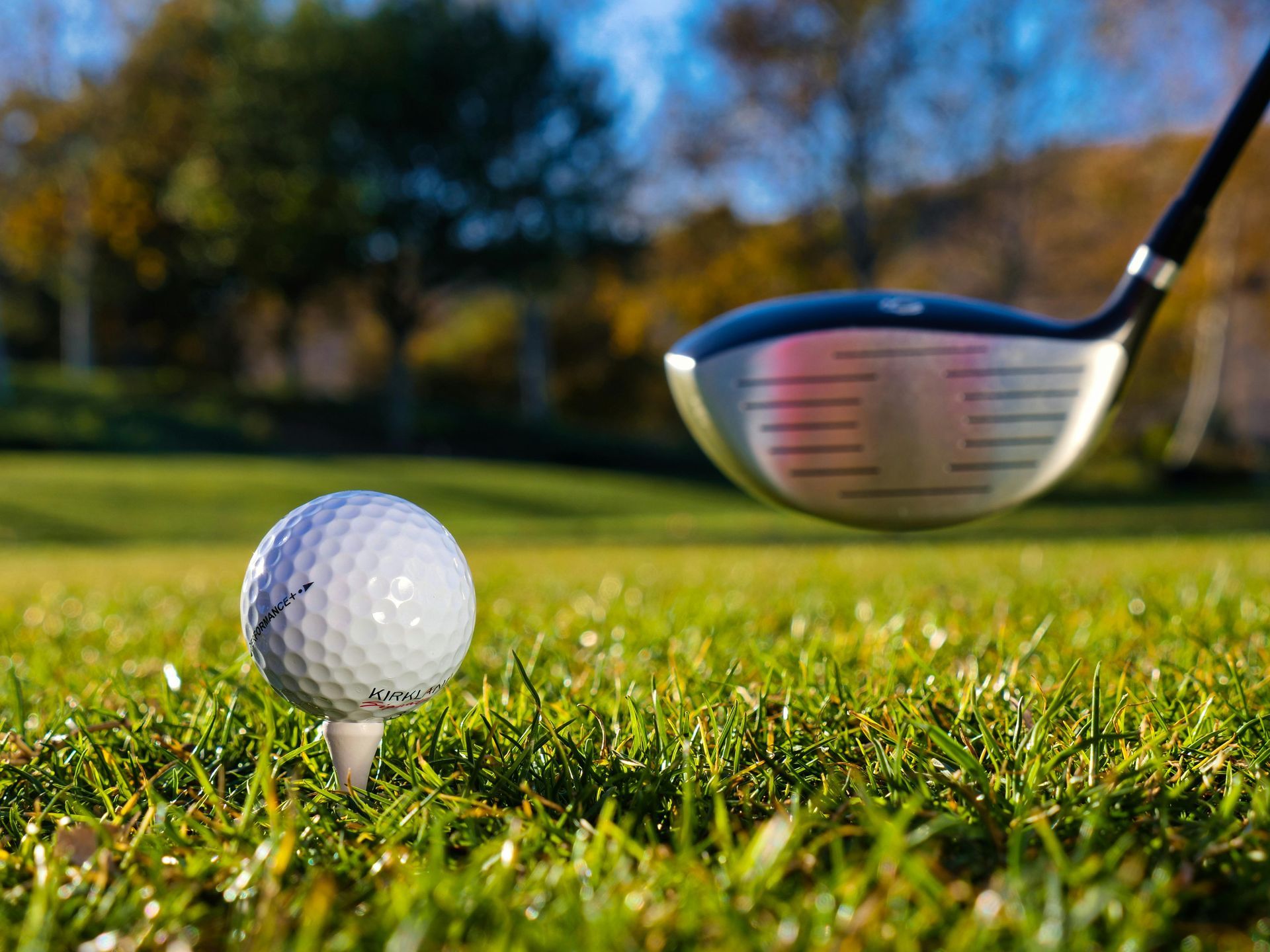 A golf ball on a tee with a golf club in the background.