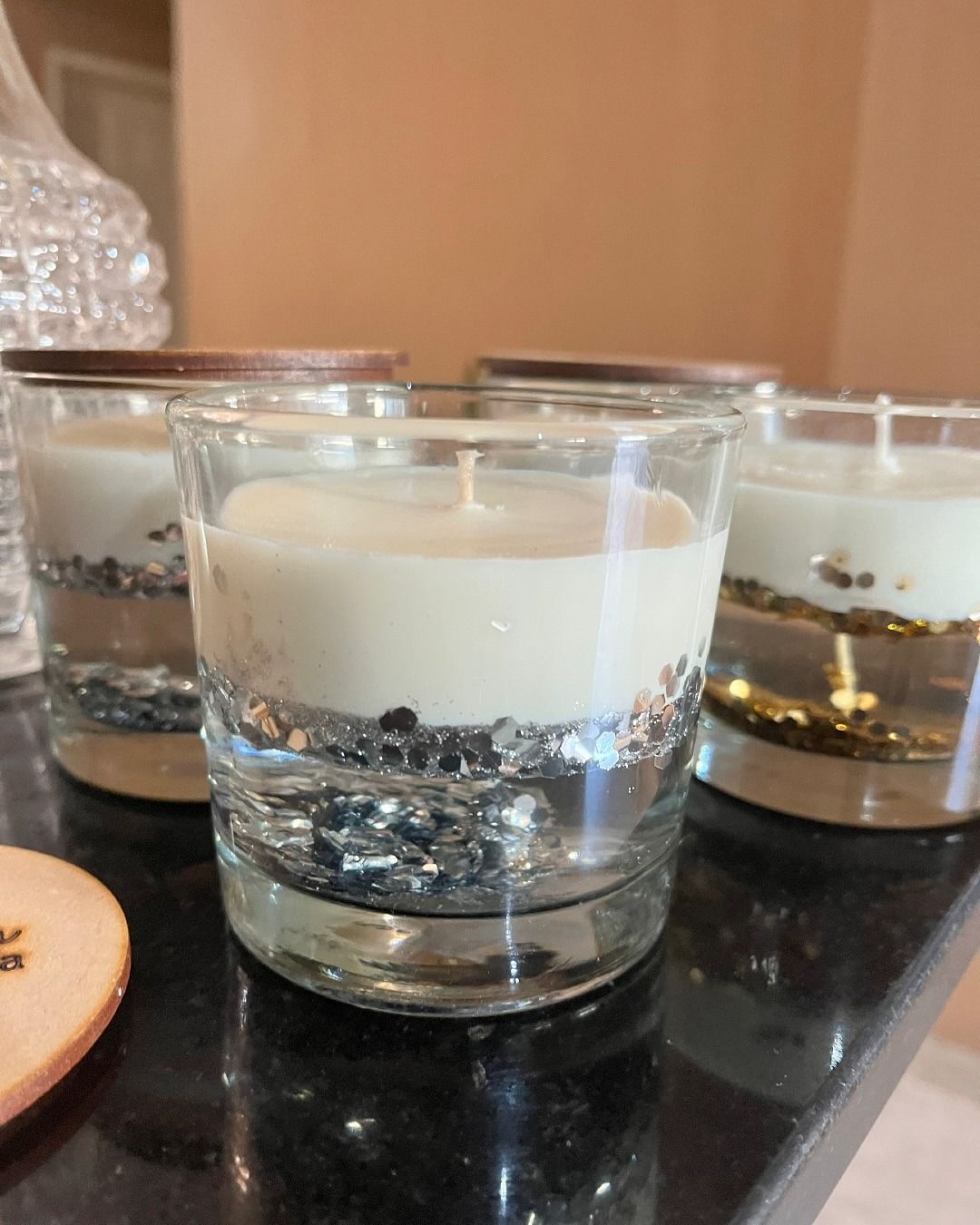 Tres velas de cristal con cera blanca y purpurina plateada sobre una mesa negra.
