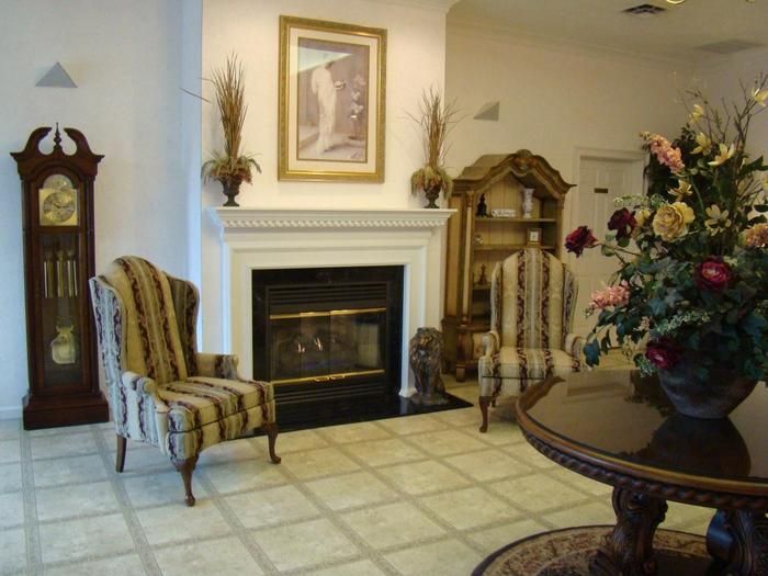 A living room with a chair , table , lamp and a picture on the wall.