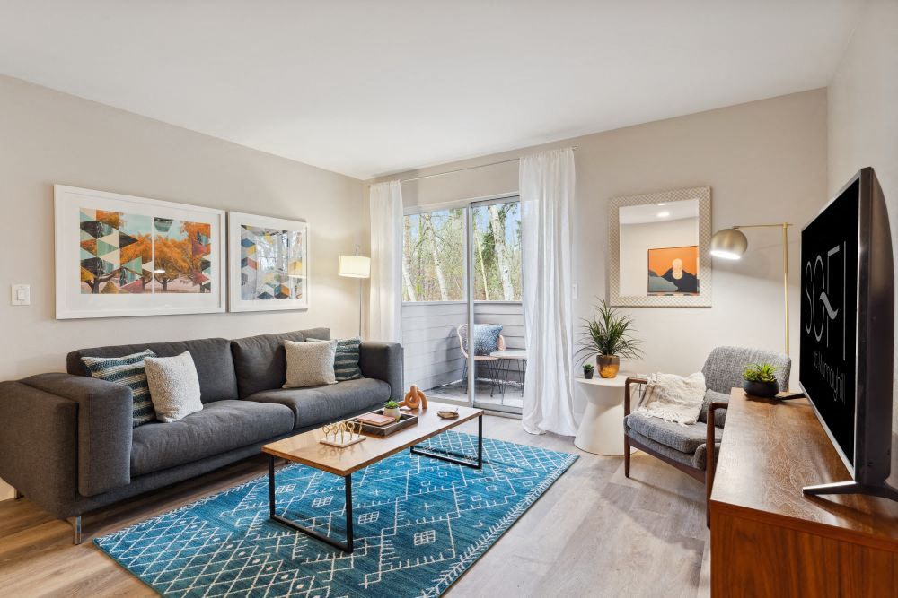 Living room in a modern apartment with a gray sofa, coffee table, and sliding glass door to a balcony at Sofi at Murrayhill, offers apartments near Murrayhill Marketplace.