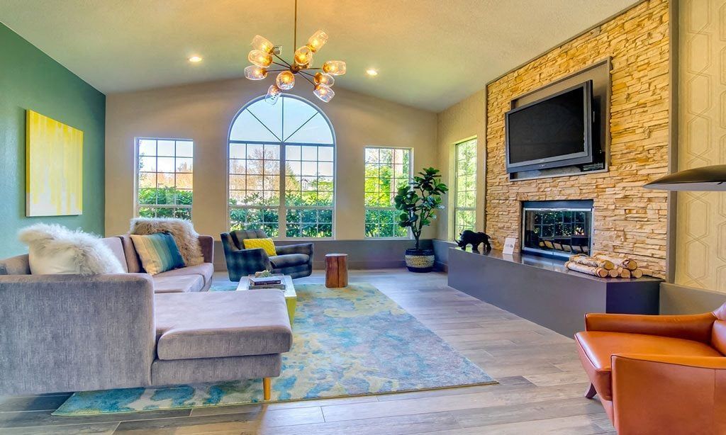 Living room in an apartment with a stone fireplace, mounted TV, and large arched window at Sofi at Murrayhill, offers apartments for rent in Beaverton, OR.