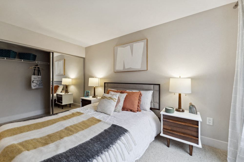 Bedroom in an apartment with a bed, two nightstands, lamps, and an open closet at Sofi at Murrayhill, offers apartments near Washington Square Mall.