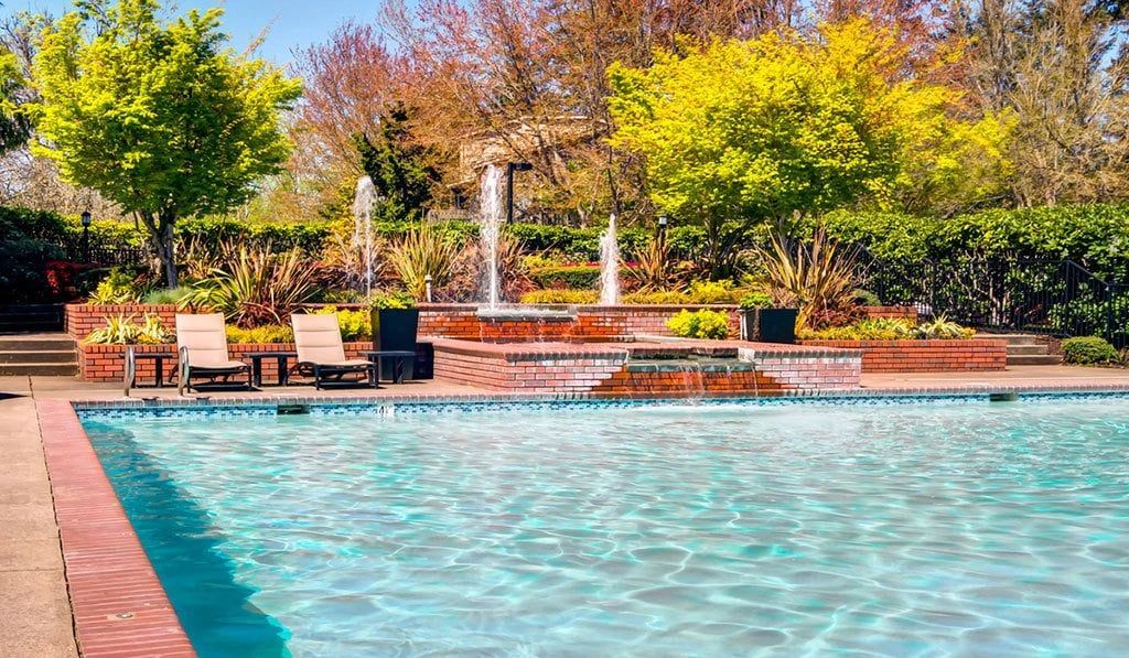 Outdoor pool area with blue water, brick edge, loungers, and landscaped surroundings at Sofi at Murrayhill, offers apartments for rent in Beaverton, OR.