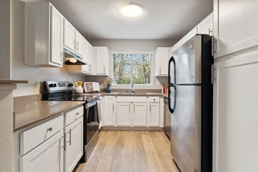 White kitchen with white cabinets, stainless-steel fridge, and a window above the sink at Sofi at Murrayhill, offers apartments in Beaverton, OR.