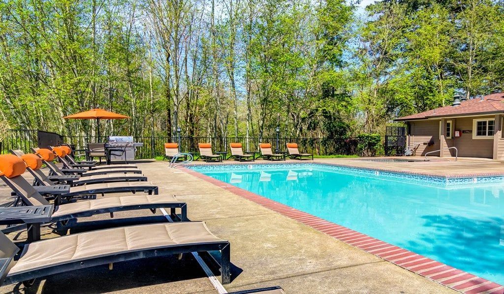 Outdoor community pool with blue water, lounge chairs, and a pool house nearby at Sofi at Murrayhill, offers apartments for rent in Beaverton, OR.