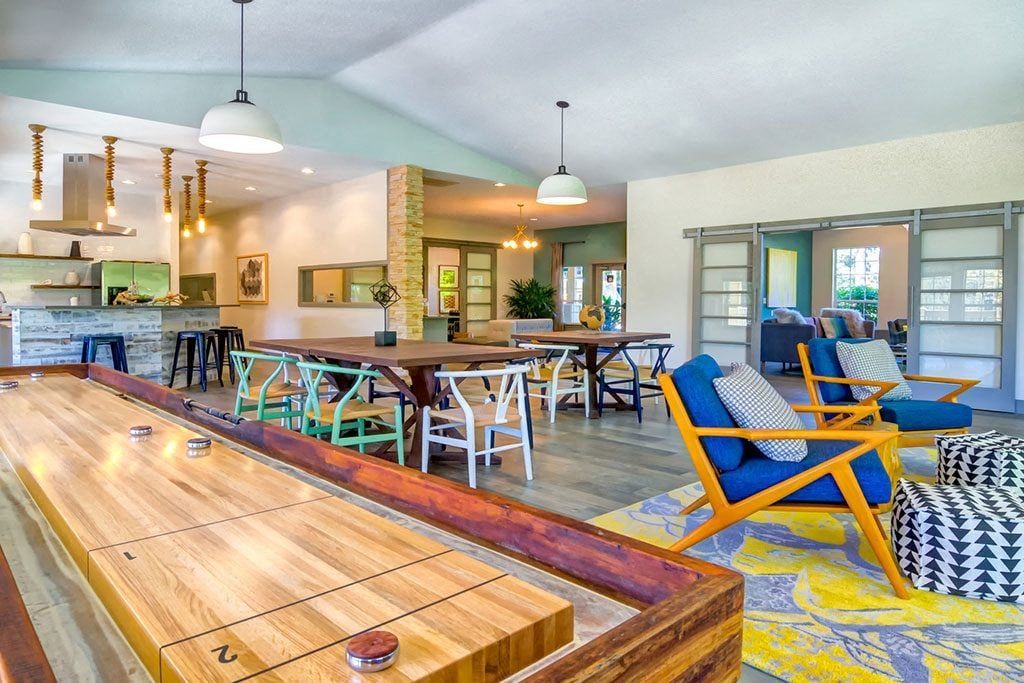 Bright communal lounge with a long wooden table, colorful chairs, and a kitchen area in the background at Sofi at Murrayhill, offers apartments for rent in Beaverton, OR.