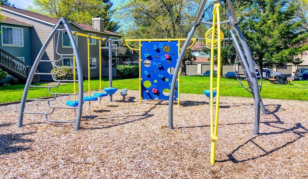Outdoor playground with metal climbing frames and a blue climbing wall in a residential complex at Sofi at Murrayhill, offers apartments for rent in Beaverton, OR.