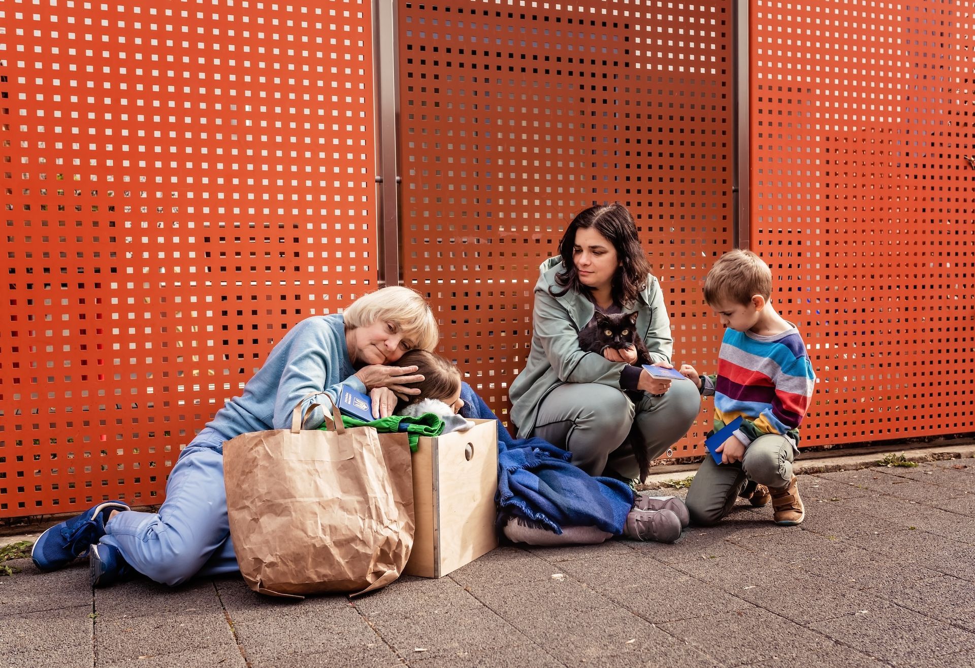 A group of people are sitting on the ground in front of an orange wall.