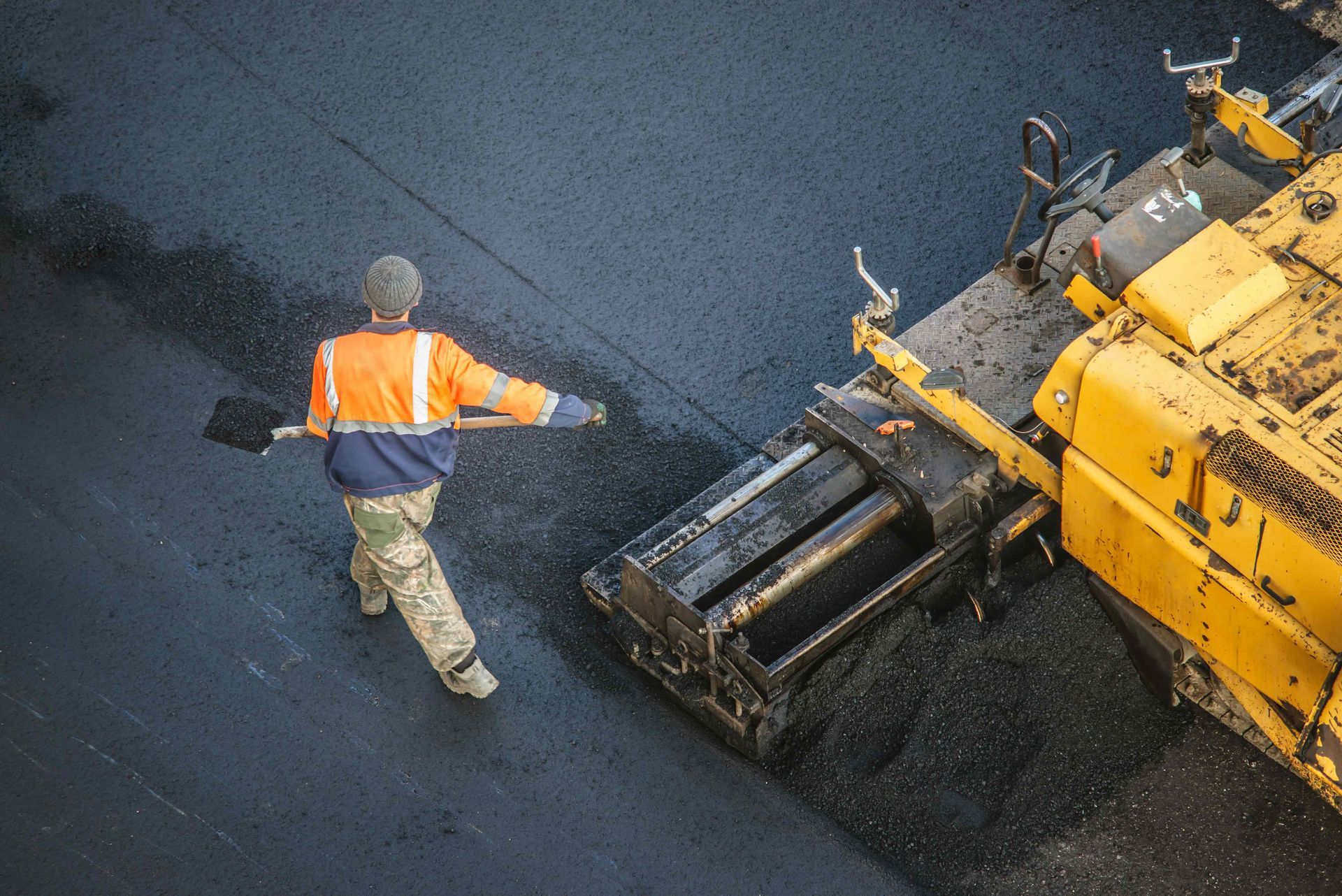 Professional asphalt paving contractor using heavy machinery and hand tools for a smooth finish.