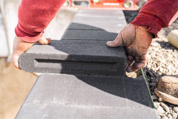 A skilled masonry professional expertly aligns black bullnose paving stones.
