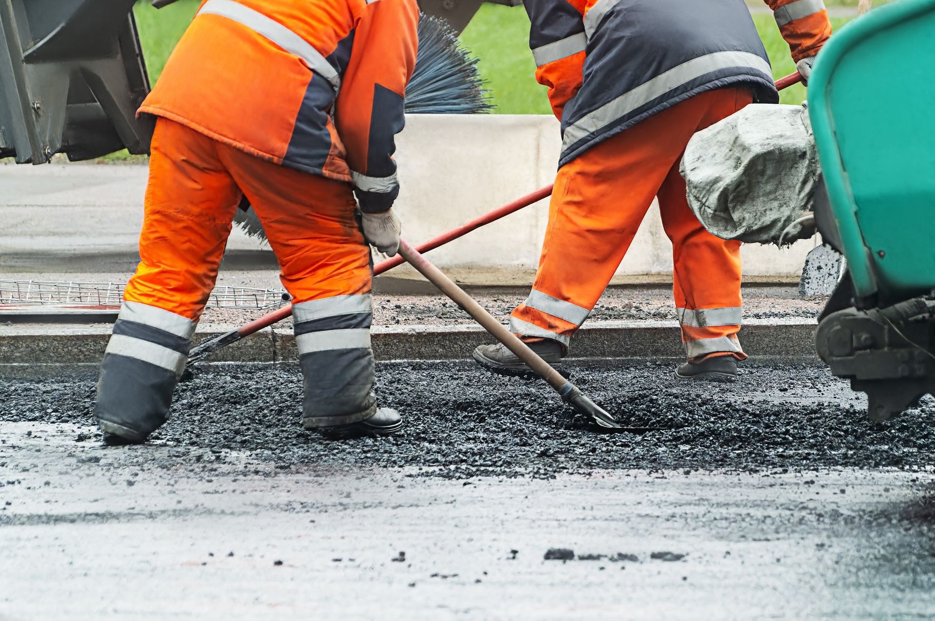 Two men in orange work clothes are shoveling asphalt - Asphalt Paving Contractor