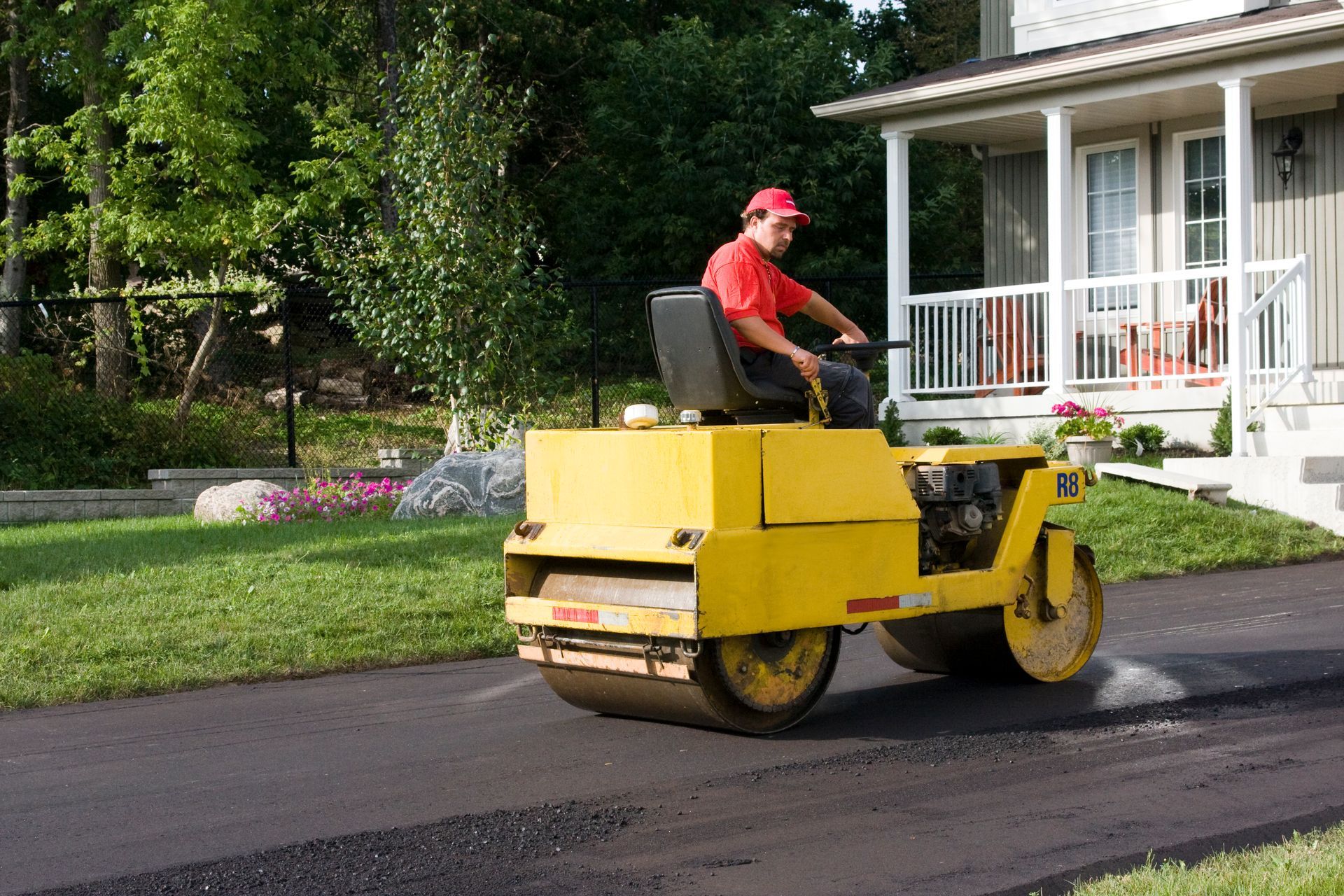 Asphalt paving contractor smoothing driveway surface with roller.