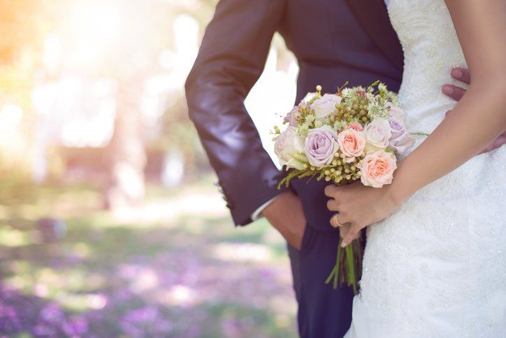 a bride and groom are standing next to each other holding a bouquet of flowers .