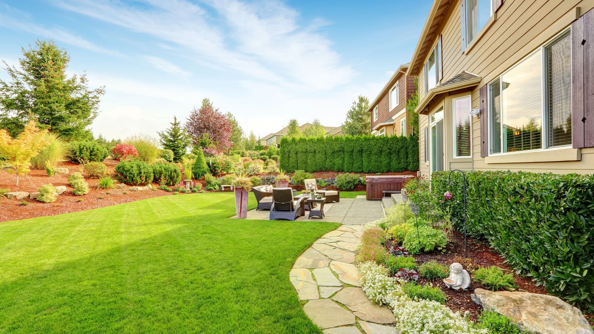 Green lawn and stone pathway in a well-landscaped backyard with a house in the background.