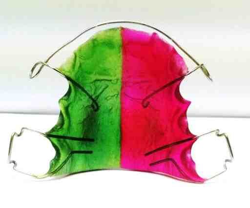 A green and pink dental retainer is sitting on a white surface.