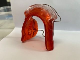 A red dental retainer is sitting on a white surface.