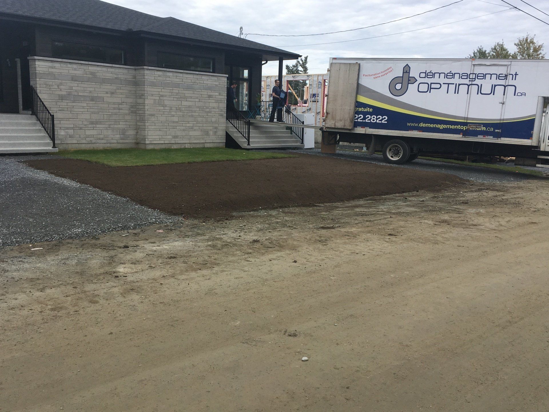 Un camion blanc avec le mot optimum dessus est garé devant une maison.