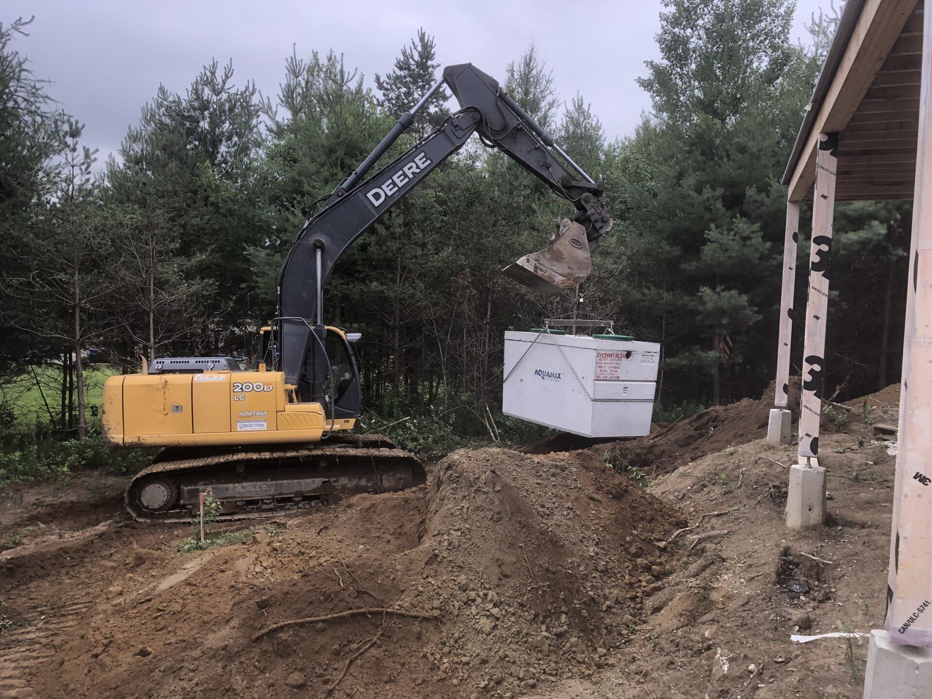 Une excavatrice Deere charge une boîte blanche dans un tas de terre.