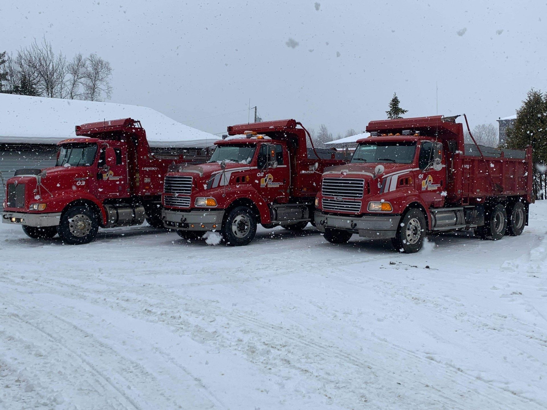 Trois camions à benne rouges sont garés dans la neige.