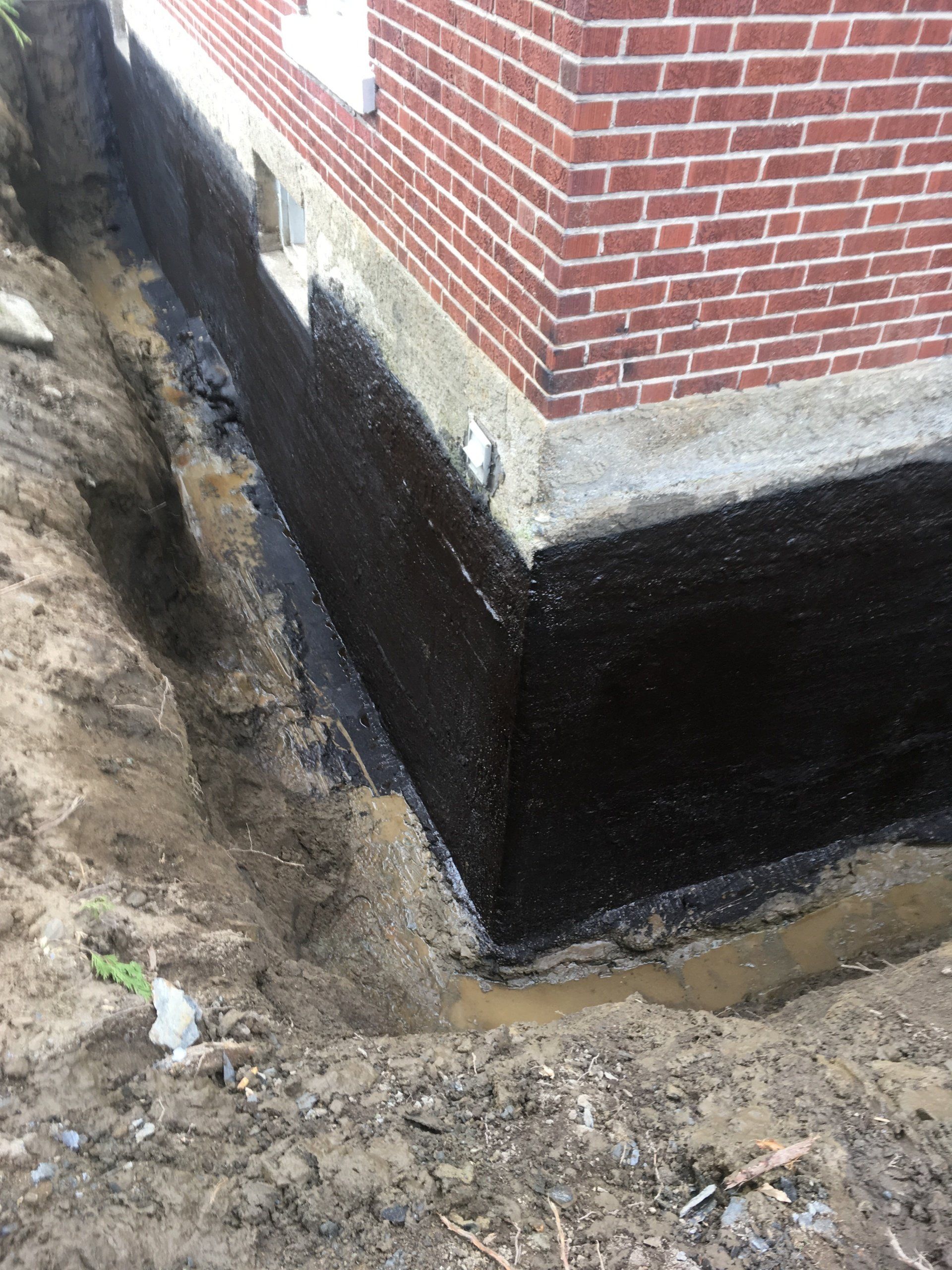 Un bâtiment en briques avec des fondations noires est en cours d'imperméabilisation.