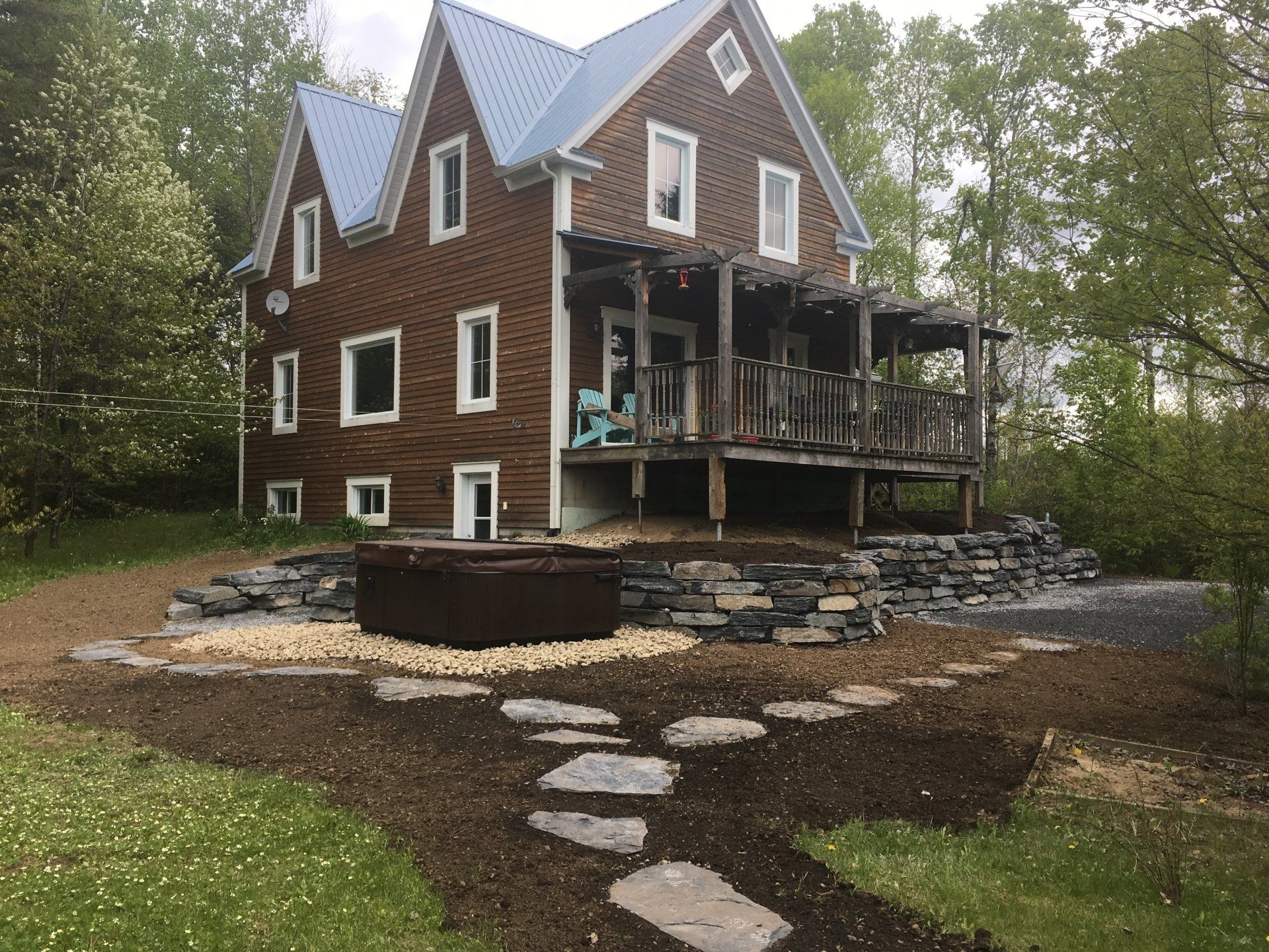 Une grande maison brune avec un toit bleu et un jacuzzi devant