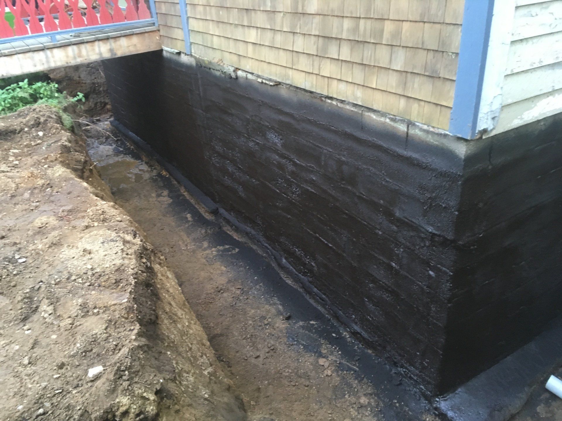 Les fondations d'une maison sont en train d'être imperméabilisées avec de la peinture noire.