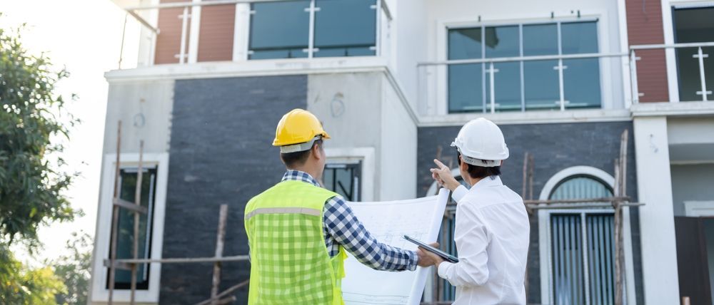 Two construction workers in hard hats reviewing plans outside a building under construction