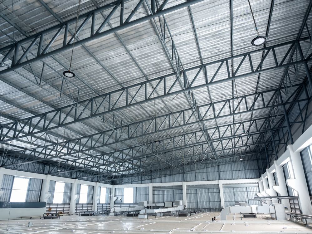 Empty industrial warehouse with steel truss ceiling and rows of windows on the left wall