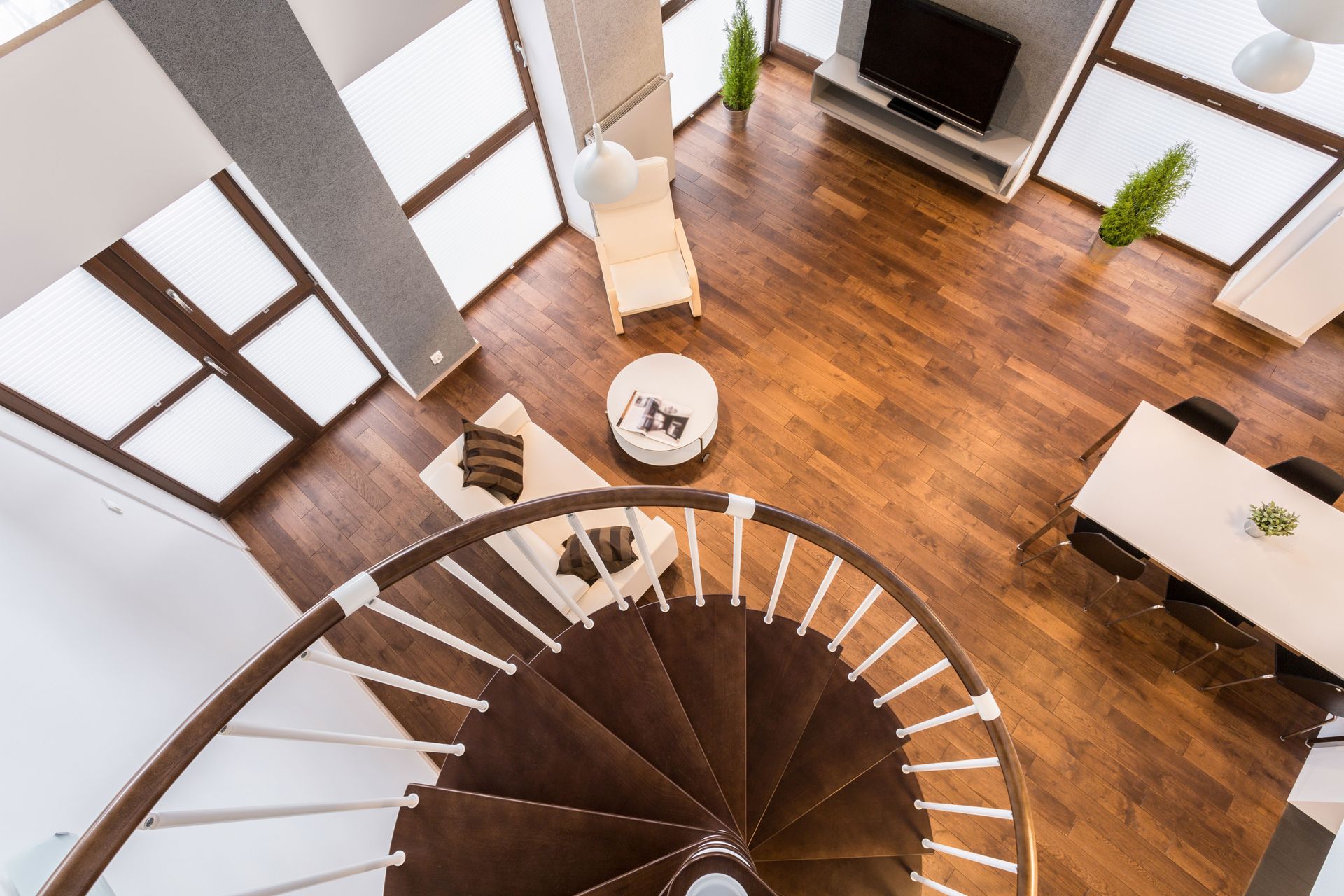 Overhead view of a modern living space with a spiral staircase, hardwood floors, and large windows.