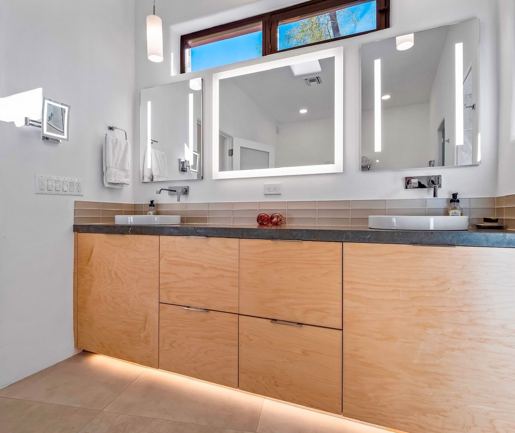 A bathroom vanity with granite countertops and a mirror that has built-in LED lights.