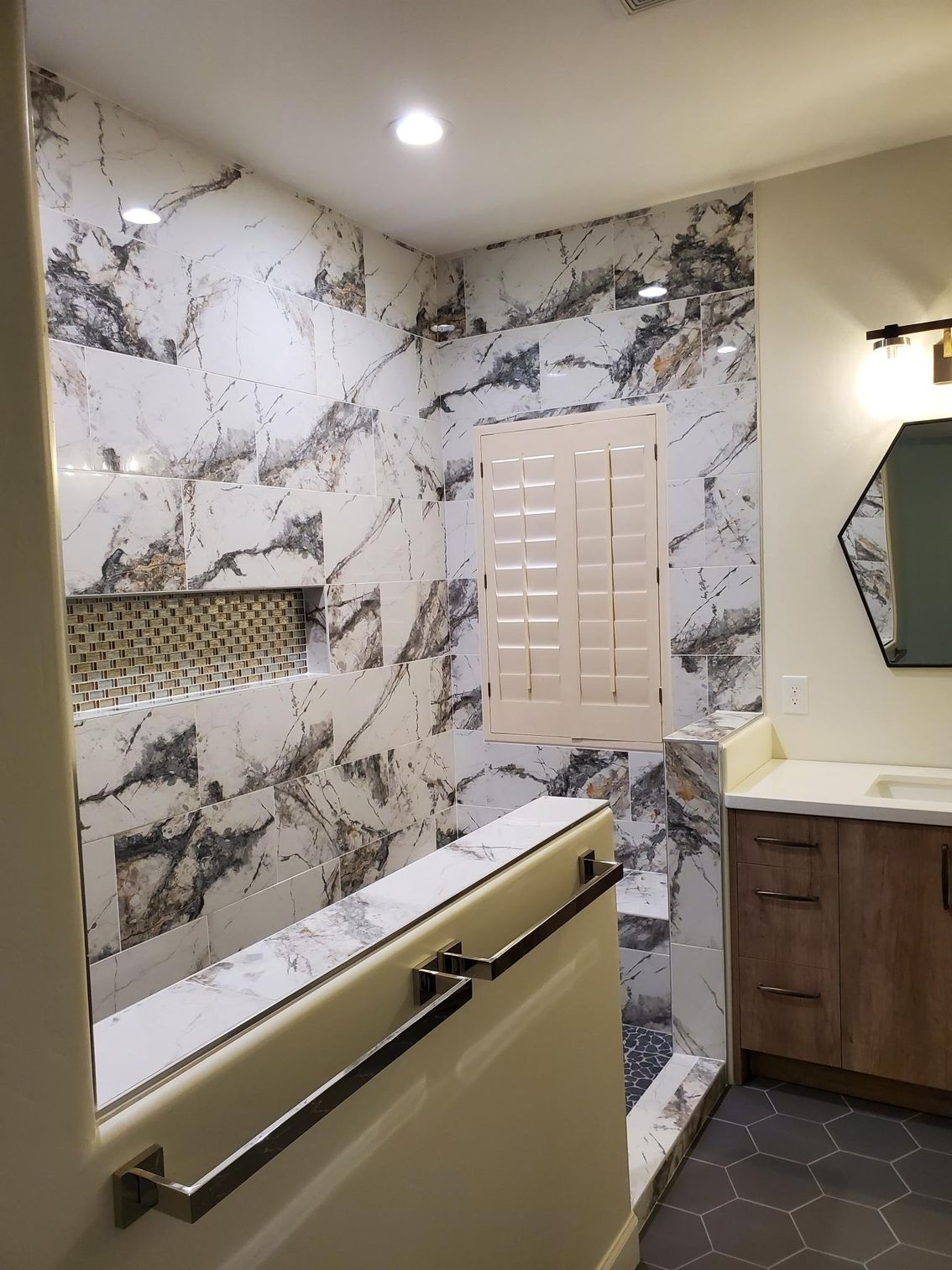 Spacious walk-in shower with marble tile walls and floor, glass door, chrome showerhead, and built-in bench.