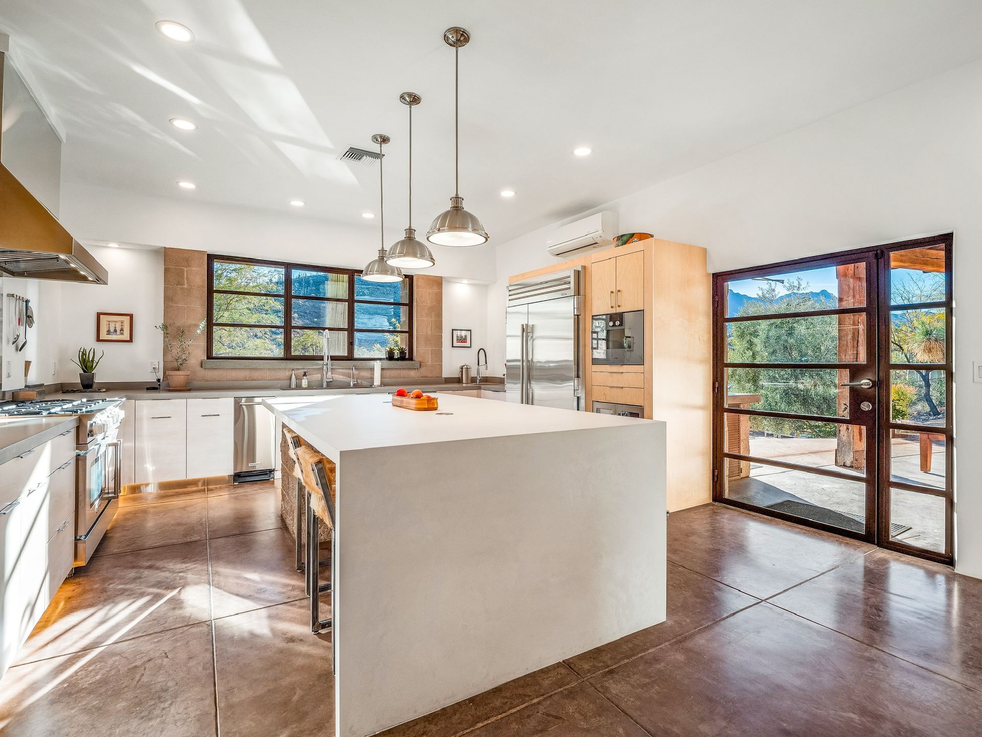 A white free-standing kitchen island features stainless steel lighting, white kitchen cabinets, and and refrigerator.