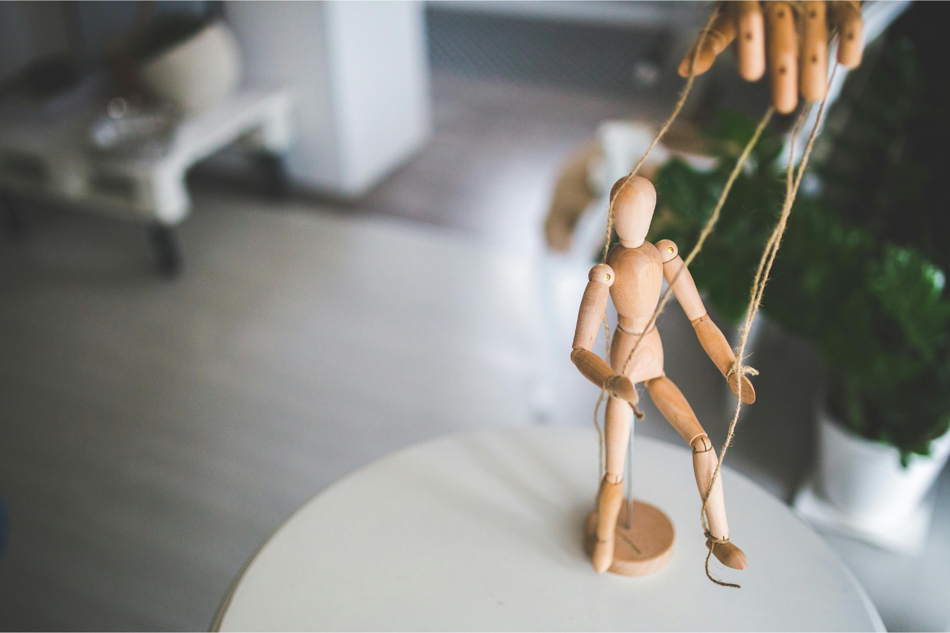 Wooden puppet being manipulated by a hand. The puppet stands on a white table.