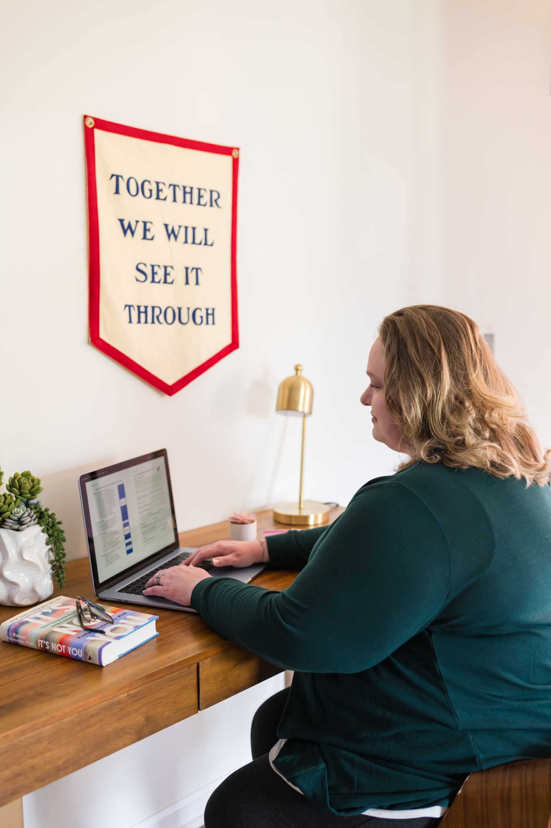 Woman typing on a laptop at a wooden desk, beneath a banner that reads