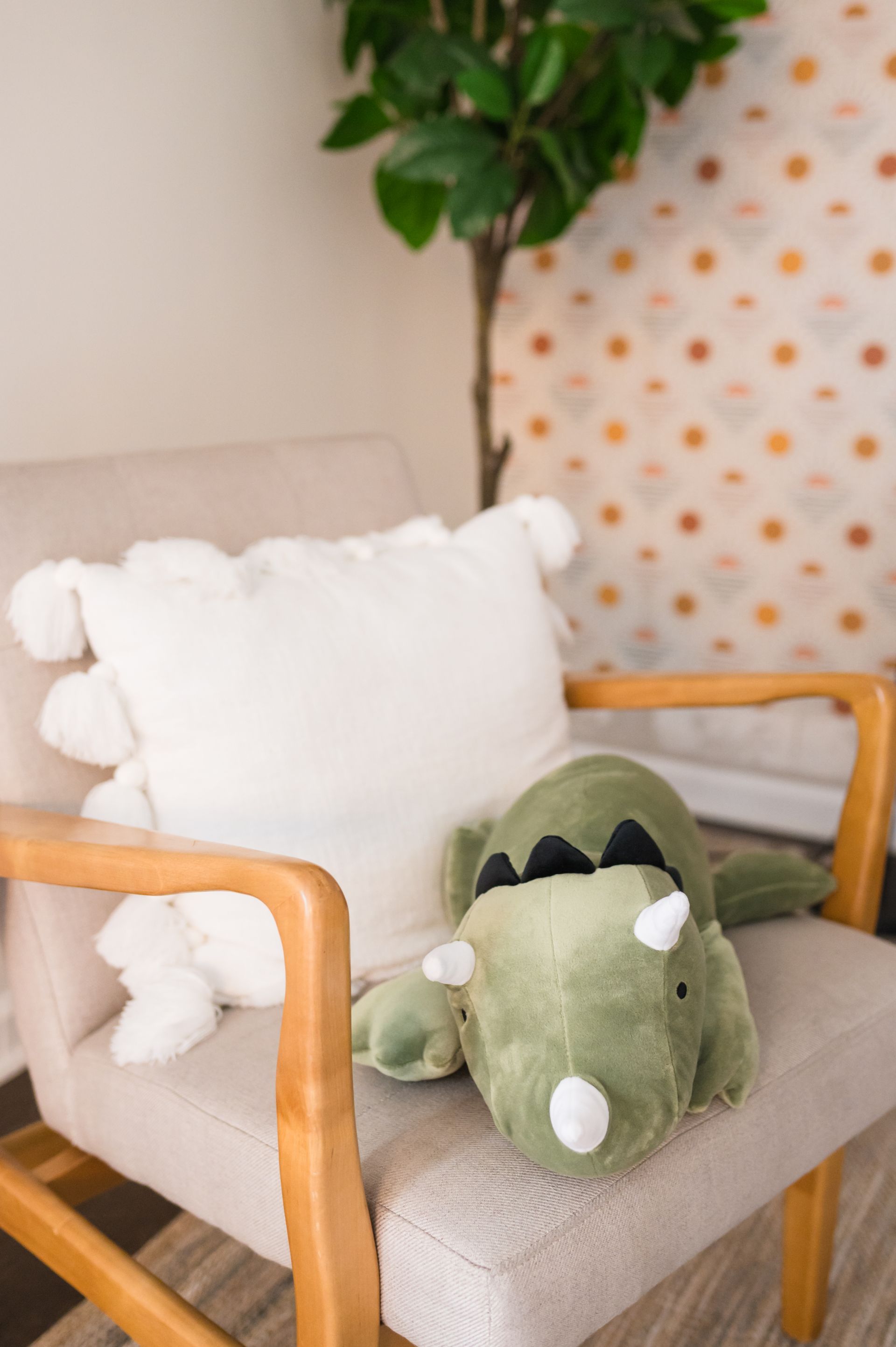 Green dinosaur plush and white pillow on a beige armchair in a room.