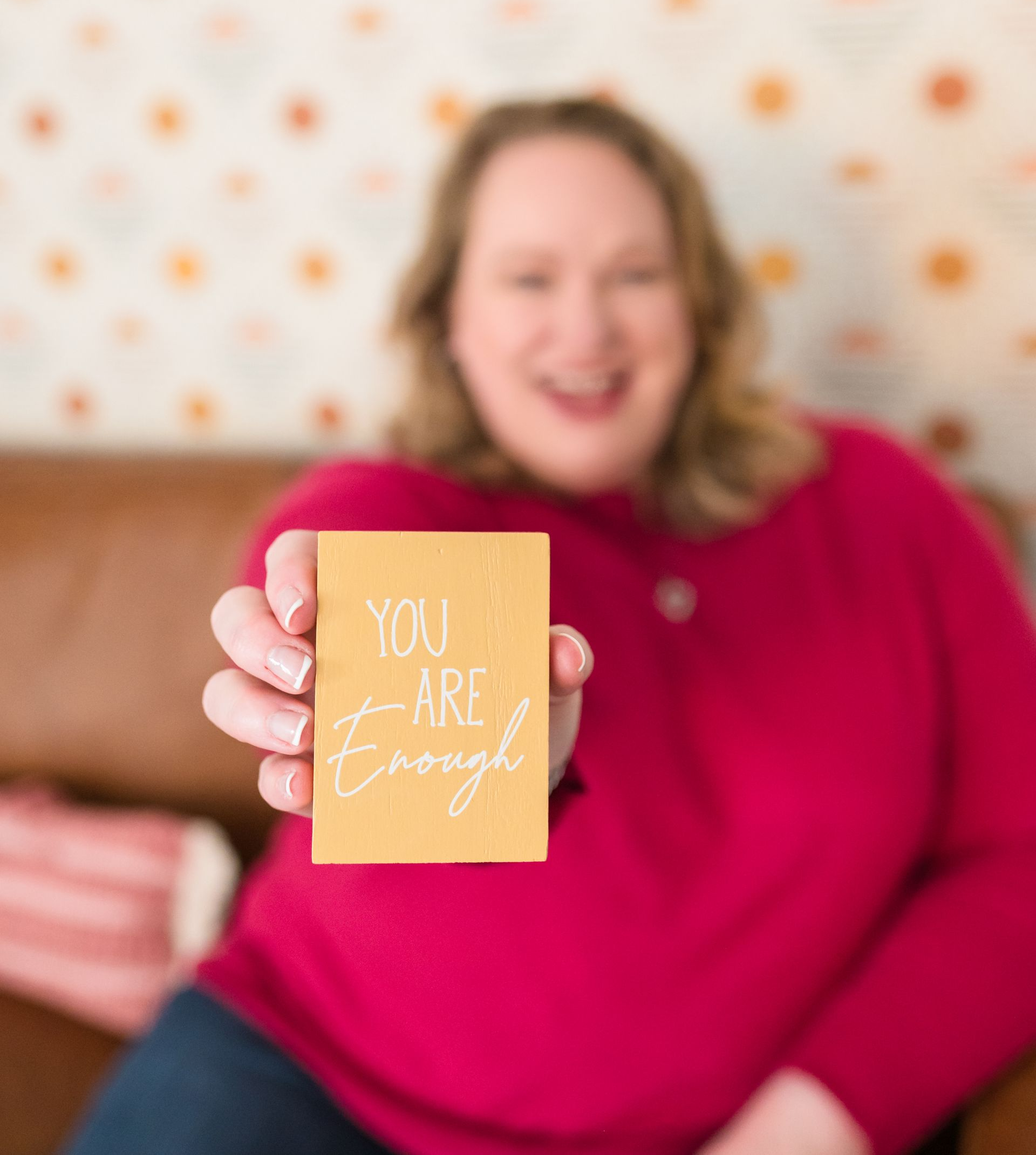 Woman in red sweater smiles, holding a yellow sign: 