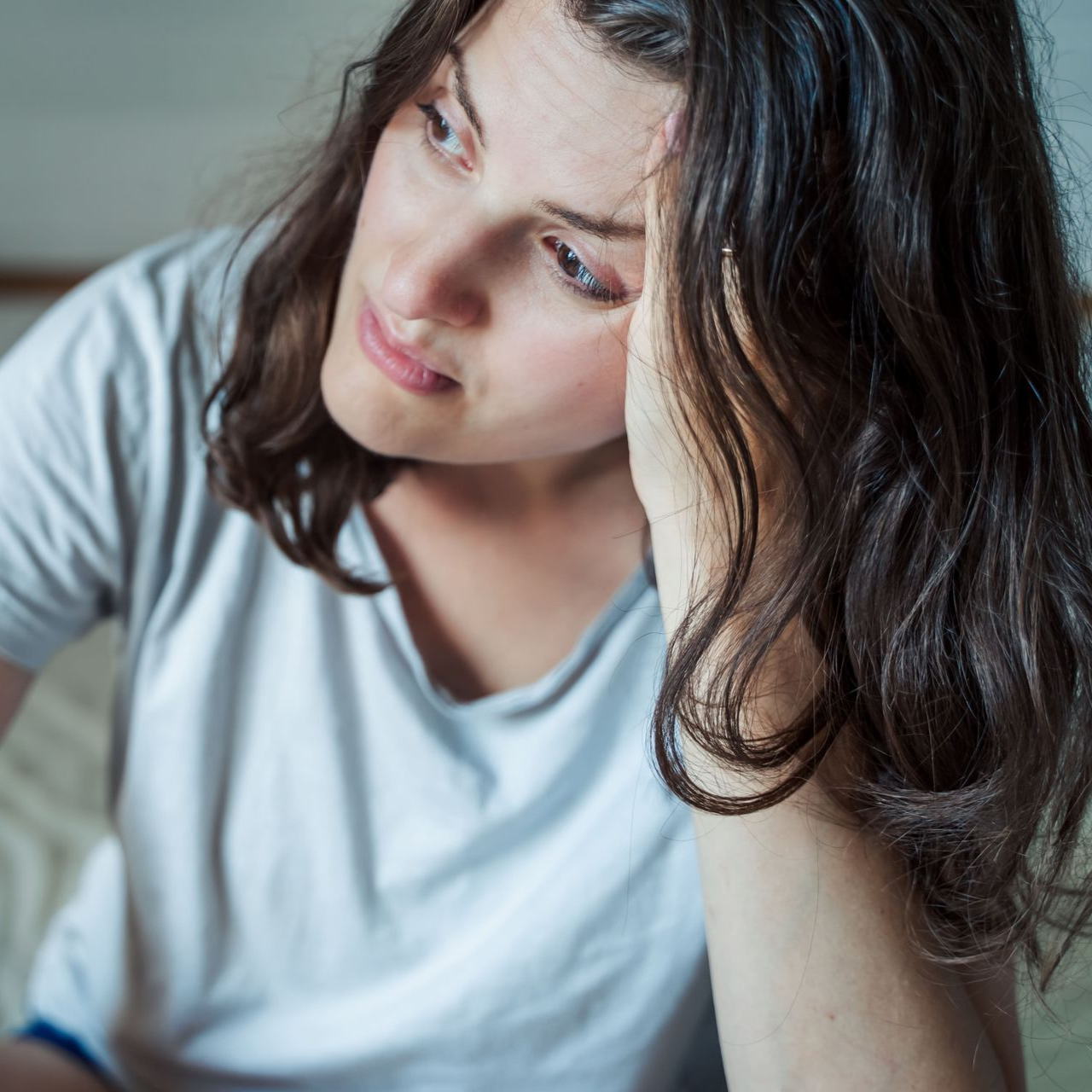 Woman with dark hair, looking thoughtful, hand on her head, in a soft-lit setting.