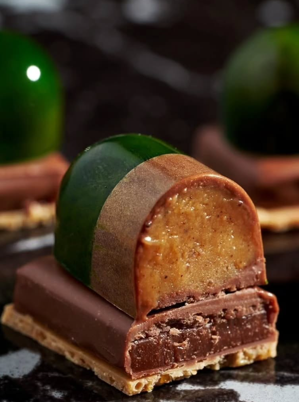 Chocolate pastry with layers of green and brown glaze, set on a dark background.