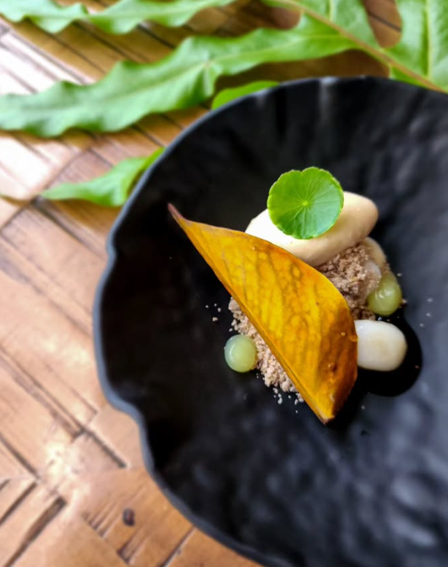 Close-up of a gourmet dessert on a black plate with a leaf garnish and brown table.