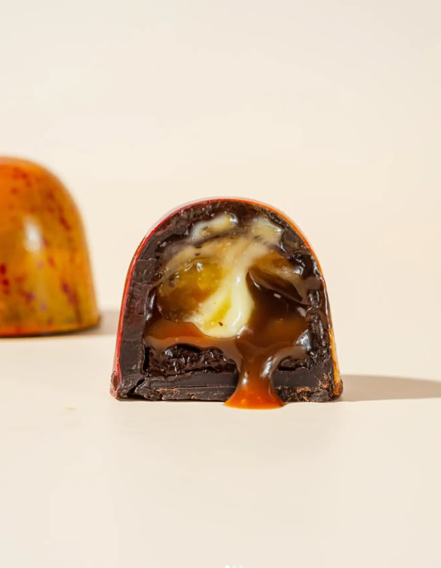 Chocolate truffle cut in half, revealing caramel, cream filling, and dark chocolate shell.